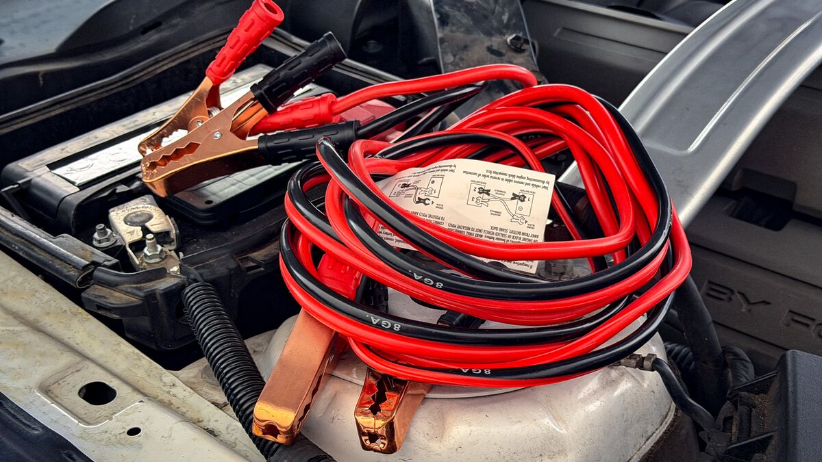 A set of jumper cables next to a car battery.