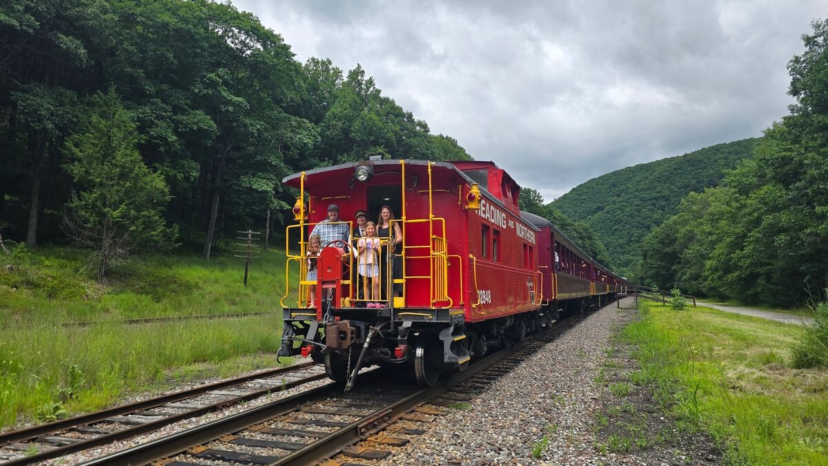A family standing on the rear platform of a caboose of a scenic railroad.