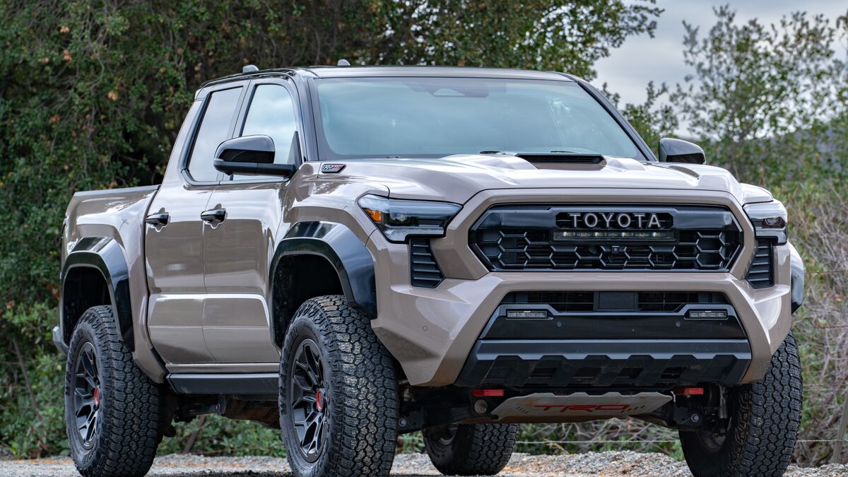 A front right-side 3/4 view of a 2026 Toyota Tacoma TRD Pro against a tree-filled backdrop under cloudy skies.