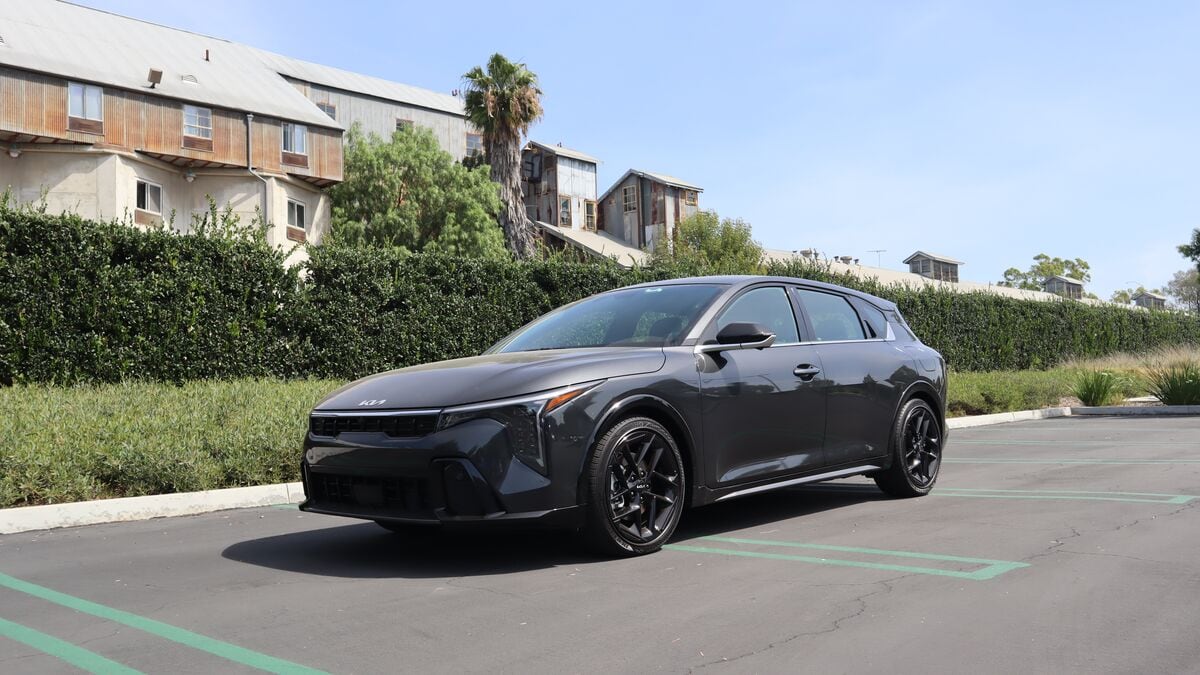 2026 Kia K4 Hatchback left-side front 3/4 view with shrubbery and a building in the background