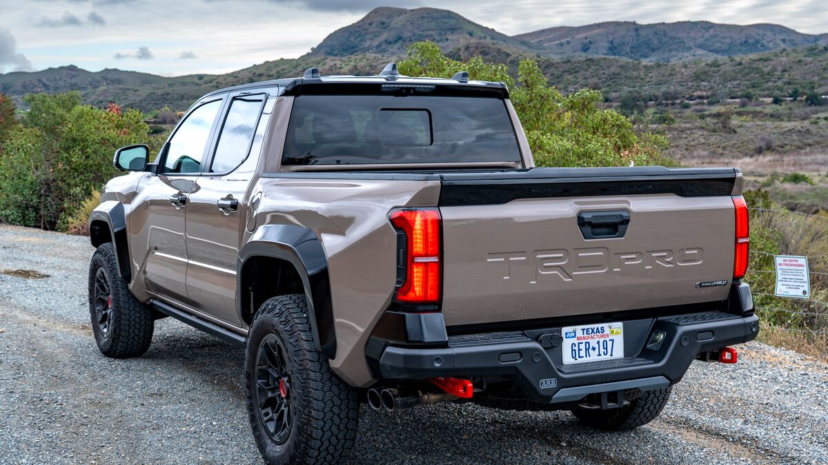 A rear left-side front 3/4 view of a 2026 Toyota Tacoma TRD Pro against a red canyon backdrop under cloudy skies.