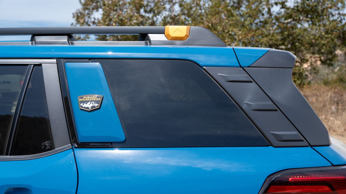 2026 Subaru Outback Wilderness rear wagon window detail on a dirt road with some green trees and brush in the background