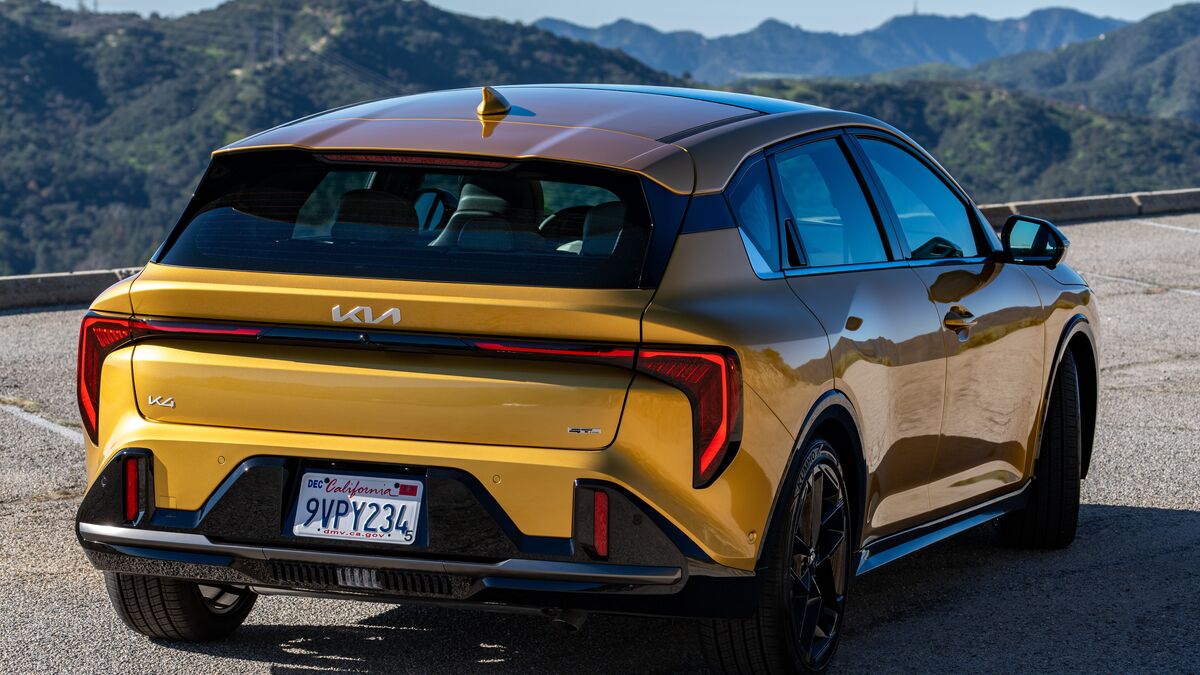 A 2026 Kia K4 hatchback in GT-Line Turbo trim and sparkling yellow paint is parked against a backdrop of the San Gabriel Mountains in a 3/4 view from the rear passenger side.