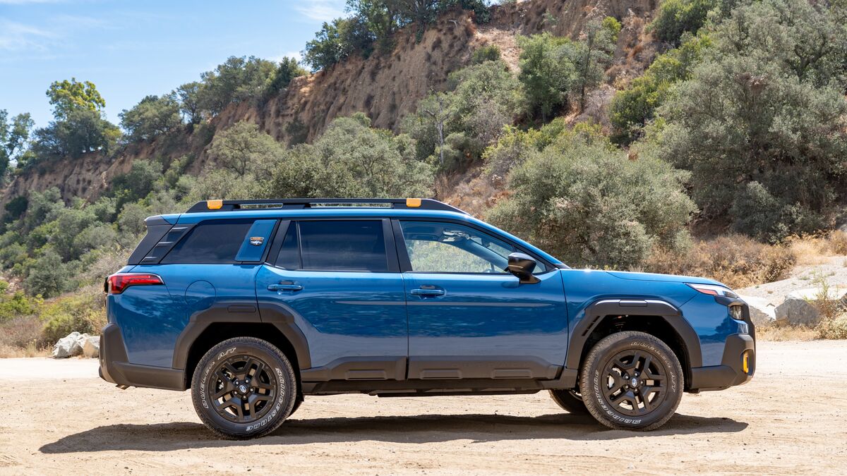 2026 Subaru Outback Wilderness right profile view on a dirt road with some green trees and brush in the background