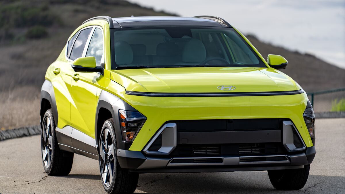 A front right-side 3/4 view of the Hyundai Kona hybrid against a grassy hillside on a cloudy day.