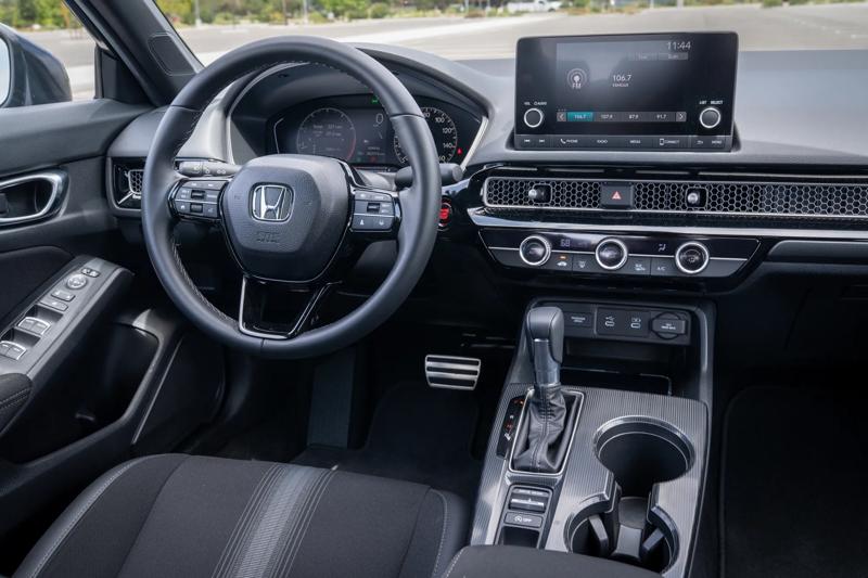 2026 Honda Civic Sport front steering wheel and dashboard with infotainment screen and console taken from the rear seats looking forward