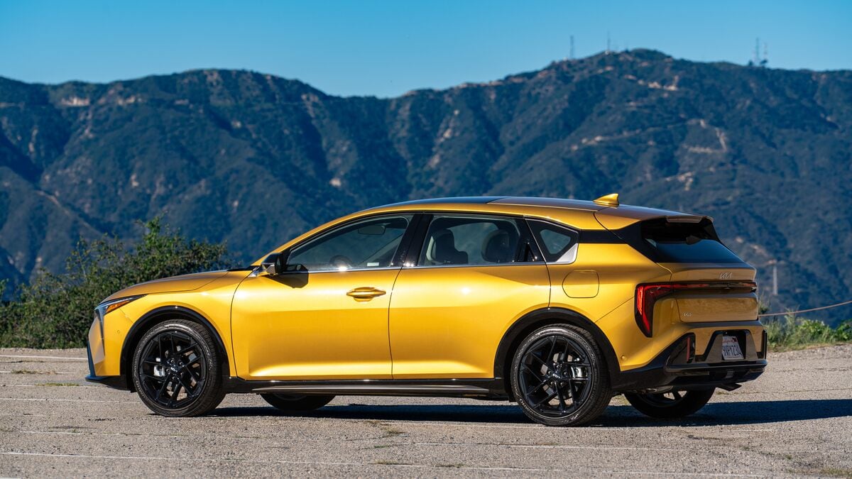 A 2026 Kia K4 hatchback in GT-Line Turbo trim and sparkling yellow paint is parked against a backdrop of the San Gabriel Mountains in a minor 3/4 view from the rear driver side.