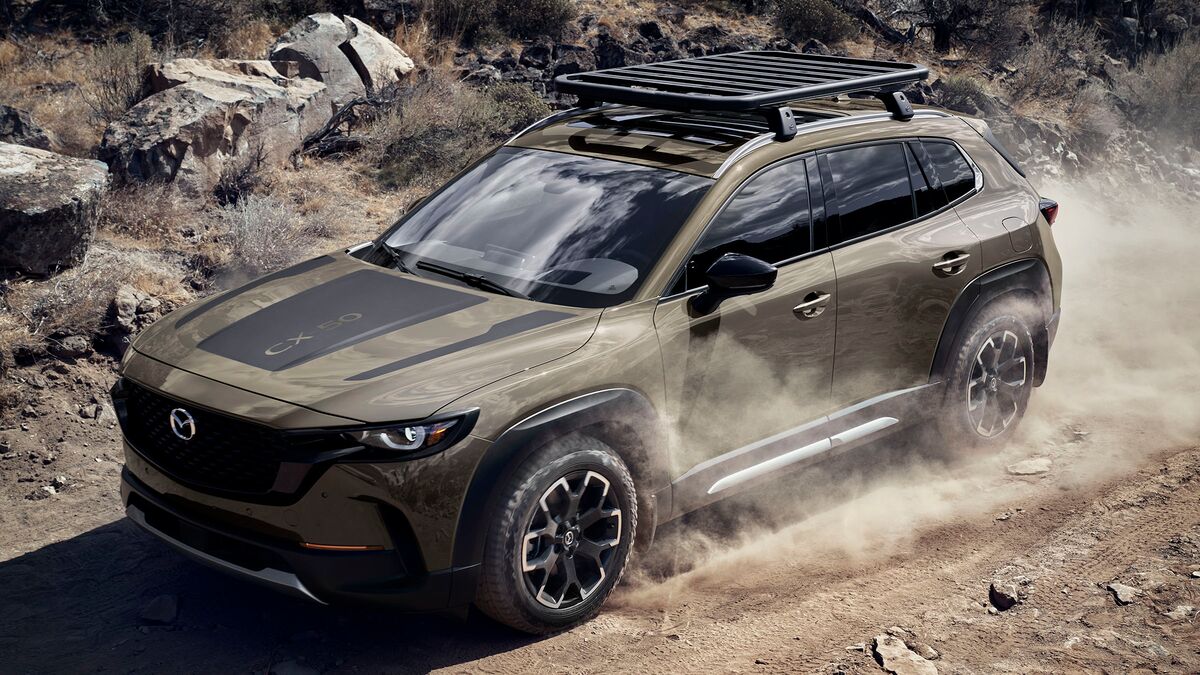 A 2026 Mazda CX 50 front 3/4 view driving on a dirt trail with a rocky background