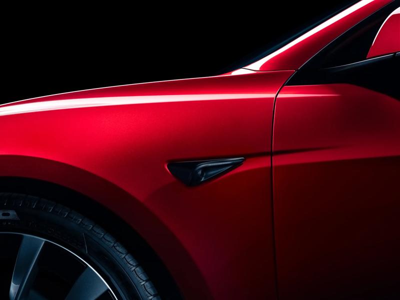 A tight shot of a red 2026 Tesla Model 3 left-hand quarter panel against a black background.