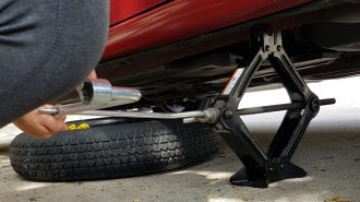 A person using a jack preparing to change a flat tire.
