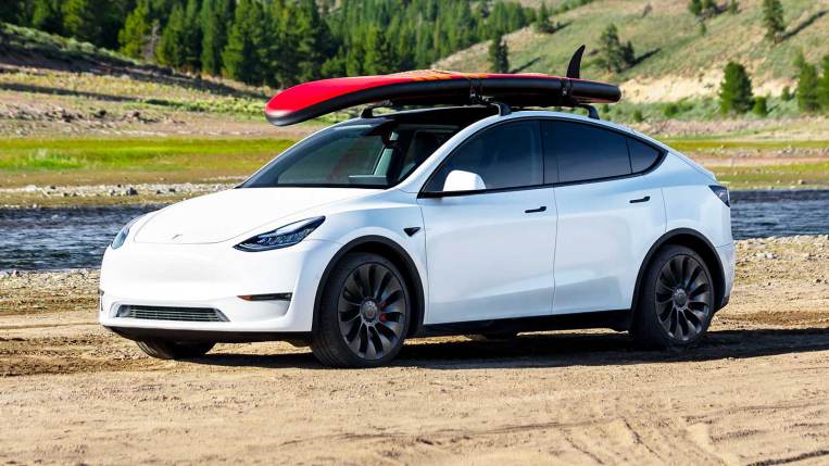 2021 Tesla Model Y in white, with a surfboard on the roof rack.