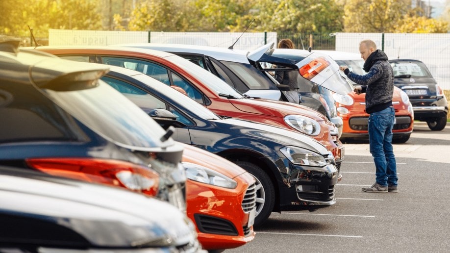 A shopper inspects the tailgate of an SUV in a used car sales lot