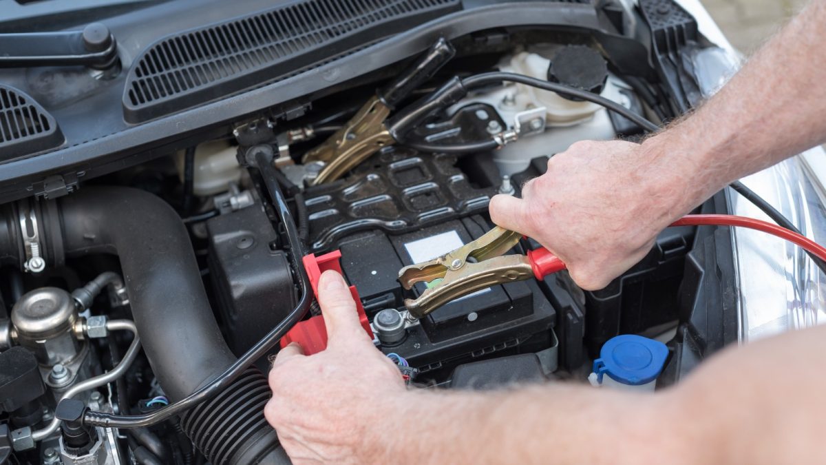 Removing the red clamp from a battery's positive terminal after jump-starting a car.