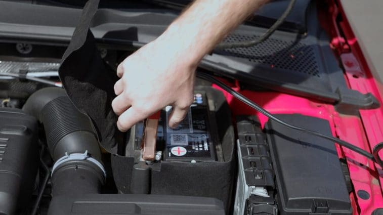 A person disconnecting the red jumper cable clamp from a car battery's positive post.