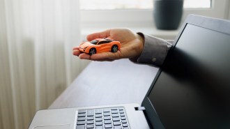 A hand holding a car by a computer.