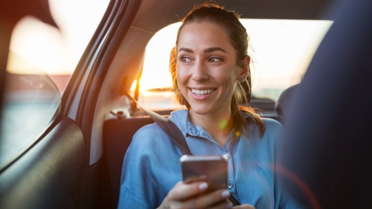 Young Woman With Smartphone In The Back Seat