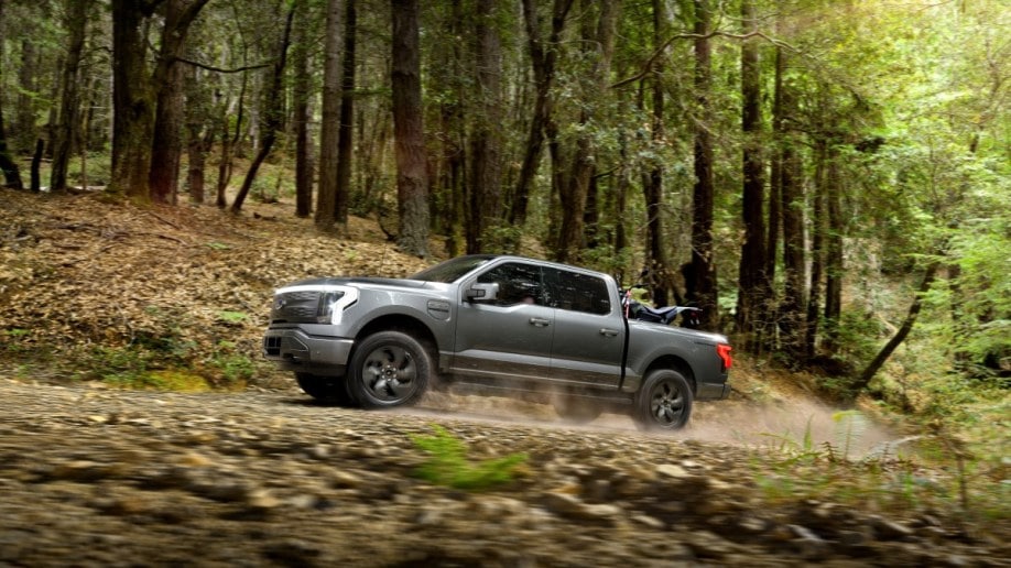 The all-electric Ford F-150 Lightning pickup drives down a forest trail