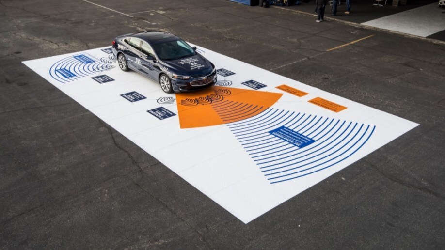 A 2016 Chevrolet Malibu is parked on a roadway painted to show the reach of its sensors detecting objects around the car