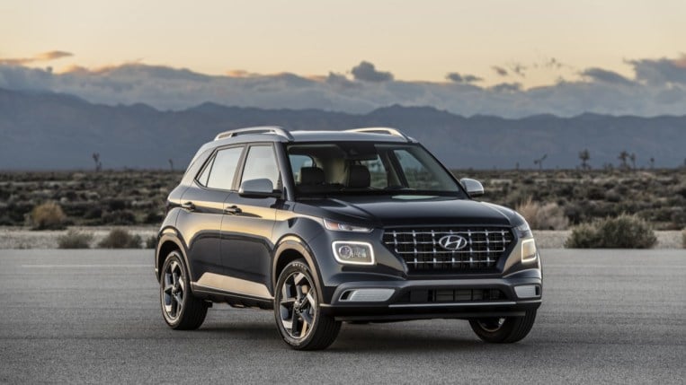 A 2022 Hyundai Venue subcompact SUV is parked against a desert backdrop. The vehicle is dark blue with a white roof. We see it from a quarter angle, facing slightly to our left.