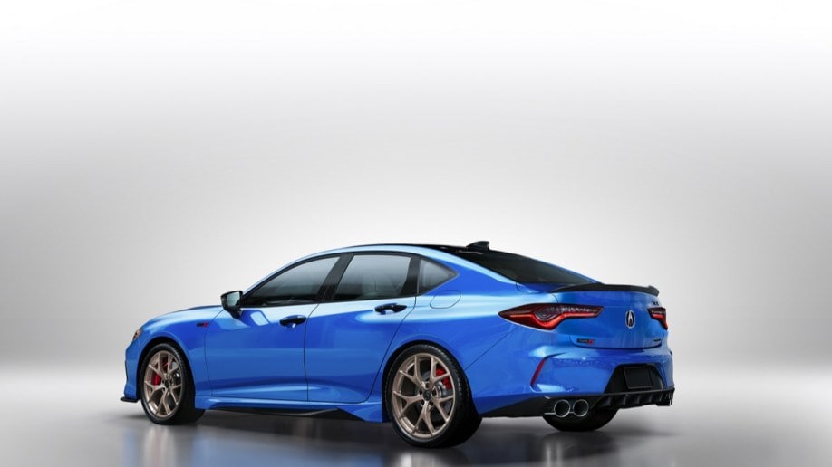 A 2023 Acura TLX Type S PMC edition sits parked against a white background. We see it from a rear quarter angle, facing our left. The car is a medium blue on copper-colored wheels.