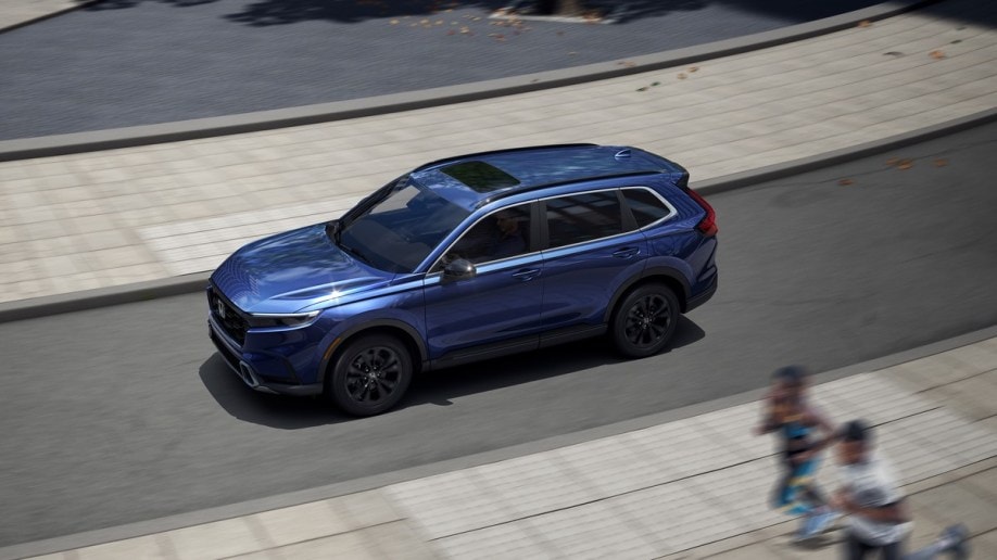 The 2023 Honda CR-V drives on a city street. We see the car in profile, from above. It is medium blue.