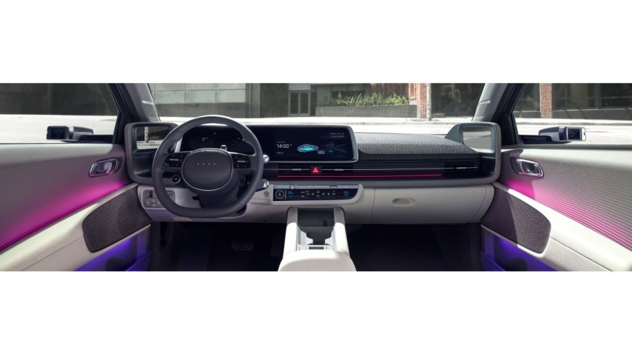 The interior of the 2023 Hyundai Ioniq 6. We see the dashboard from between the front seats. The cabin is upholstered in an off-white and light gray scheme, with purple ambient lighting.
