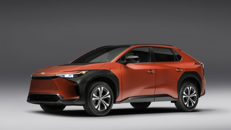 A 2023 Toyota bZ4X sits parked against a gray backdrop. It is red, with black body cladding around its wheels. We see it in profile, facing to our left.