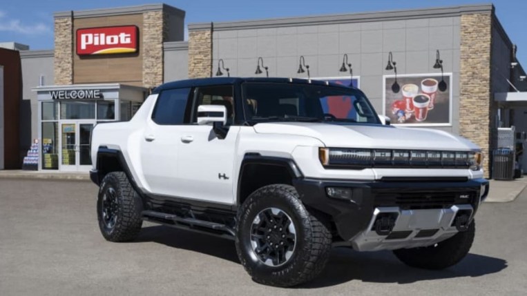 A GMC Hummer EV is parked in front of a Pilot travel center convenience store. The truck is white. We see it from a front quarter angle, facing to our right.