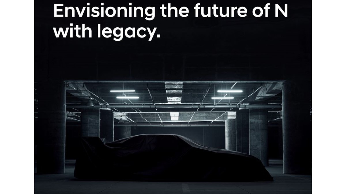 A mystery car sits under a sheet in a parking garage. It seems to have the long, low lines of a sports coupe, and a high rear wing. Above it, text reads "Envisioning the future of N with Legacy"