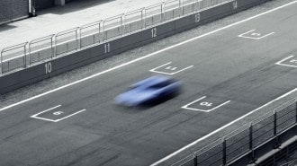 A deliberately blurred photo of a hatchback on a race track. We see the car from overhead. It appears in a shade of light blue Hyundai often uses to market its high-performance vehicles.