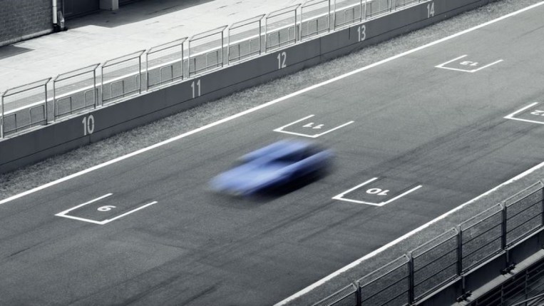 A deliberately blurred photo of a hatchback on a race track. We see the car from overhead. It appears in a shade of light blue Hyundai often uses to market its high-performance vehicles.