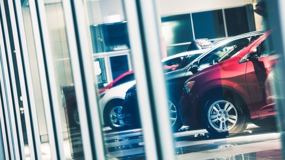 A line of cars seen through a dealership window.