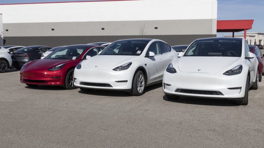 A line of Tesla Model 3 sedans sits parked outside a Tesla dealership.