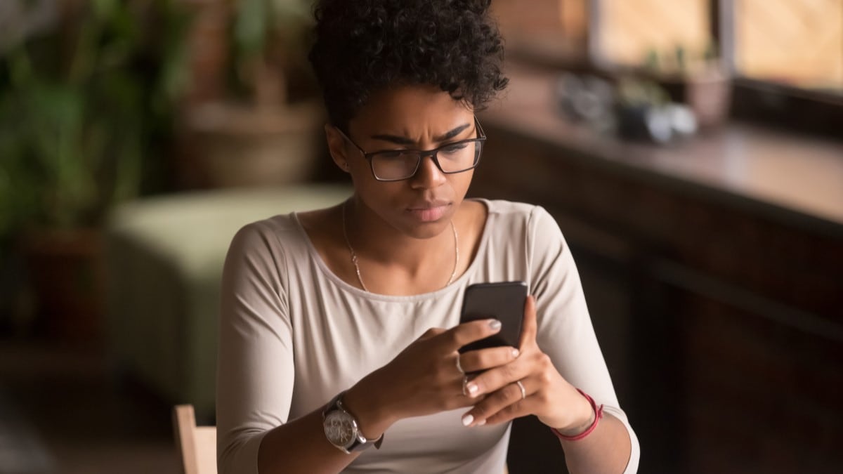 A woman stares at her cell phone in evident annoyance.