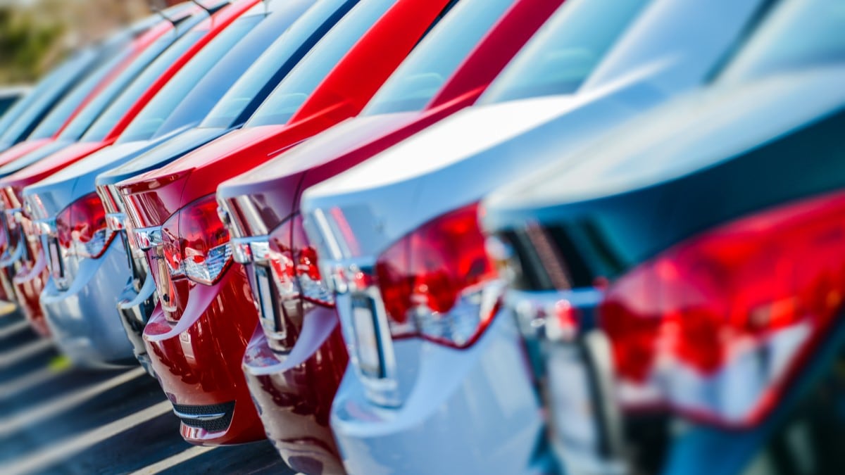 A line of small cars for sale at a car dealership in a rainbow of colors. We see just their rear lights.