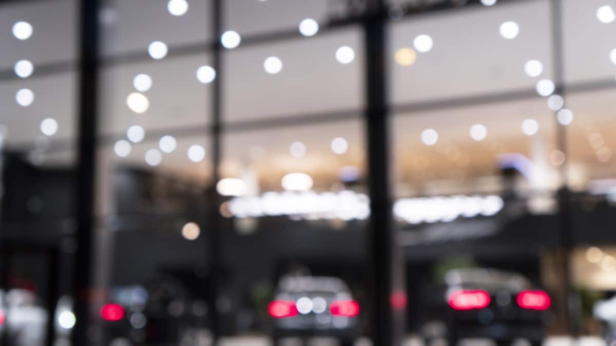 A car dealership's sales lot seen through a window. It is night and the lot is lit by fairy lights.