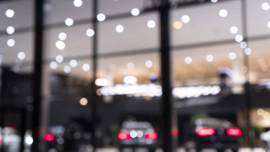 A car dealership's sales lot seen through a window. It is night and the lot is lit by fairy lights.
