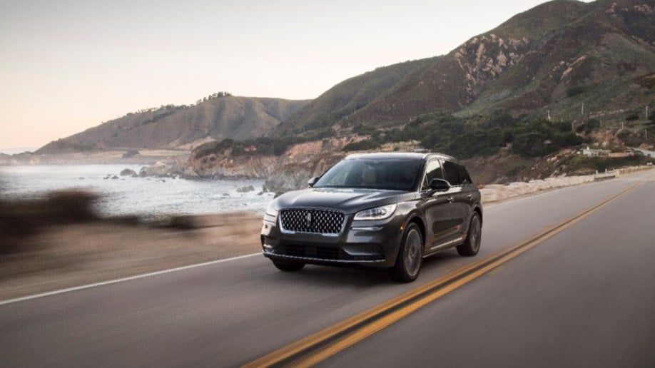 The Lincoln Corsair small SUV drives past a rocky shoreline. We see the vehicle from a front quarter angle, facing slightly to our left.