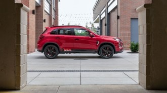 A 2022 Mitsubishi Outlander Sport sits parked between brick buildings. It is red. We see it in profile.