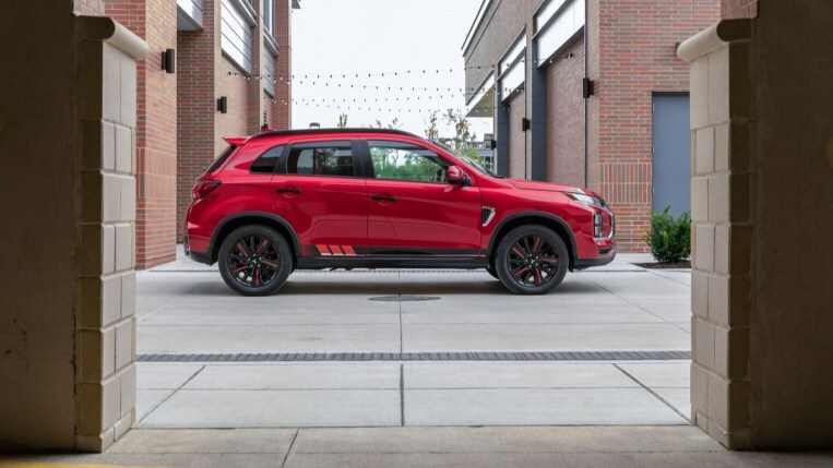 A 2022 Mitsubishi Outlander Sport sits parked between brick buildings. It is red. We see it in profile.