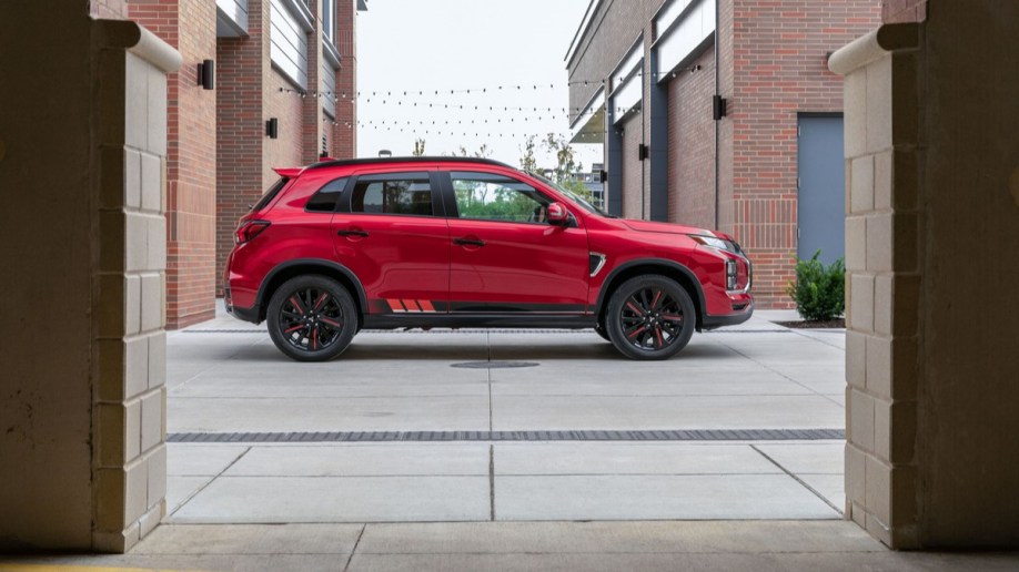 A 2022 Mitsubishi Outlander Sport sits parked between brick buildings. It is red. We see it in profile.