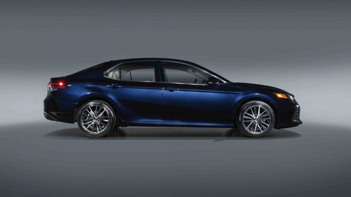 The 2022 Toyota Camry sits parked against a gray backdrop. The car is a dark shade of blue. We see it in profile, facing our right.