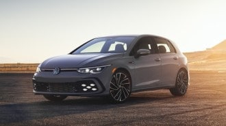 The 2022 Volkswagen Golf GTI in gray. We see it from a front quarer angle, with a setting sun behind,
