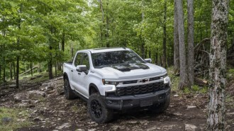 The 2023 Chevrolet Silverado ZR2 Bison parked in the woods. The truck is white with a black power bulge in the hood