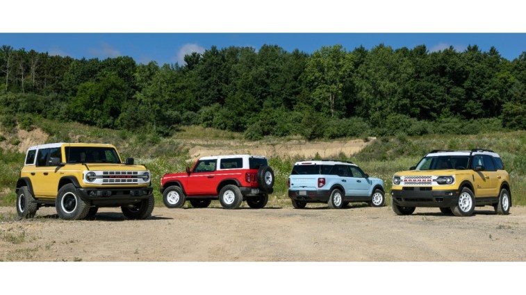 The full lineup of Ford Bronco and Bronco Sport Heritage Editions sits parked in front of a forest. From left to right, we see a yellow 4-door Bronco Heritage Limited Edition, a red 2-door Bronco Heritage Edition, a Robin's Egg Blue Bronco Sport Heritage Limited Edition, and a yellow Bronco Sport Heritage Edition.