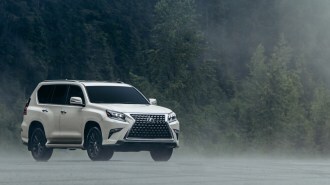 The 2023 Lexus GX sits in front of an evergreen forest in fog. The SUV is white. We see it from a front quarter angle, facing slightly to our right.