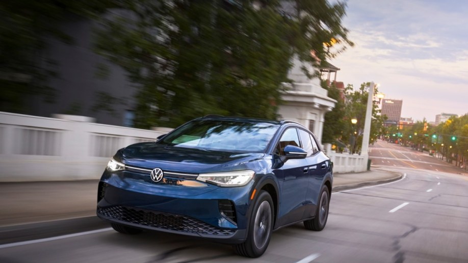 The 2023 Volkswagen ID.4 drives down a city street. The crossover is medium blue. We see it from a front quarter angle, facing slightly to our left.