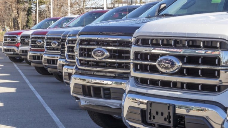 A line of Ford Super Duty trucks for sale on the dealer's lot. We only see their grills.