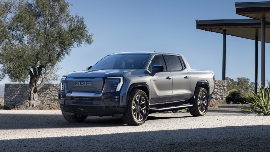 Silver 2024 GMC Sierra EV Denali Edition parked near tree.