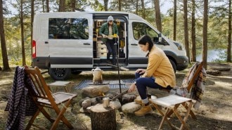 The Ford Transit Trail van in profile with campers in the woods